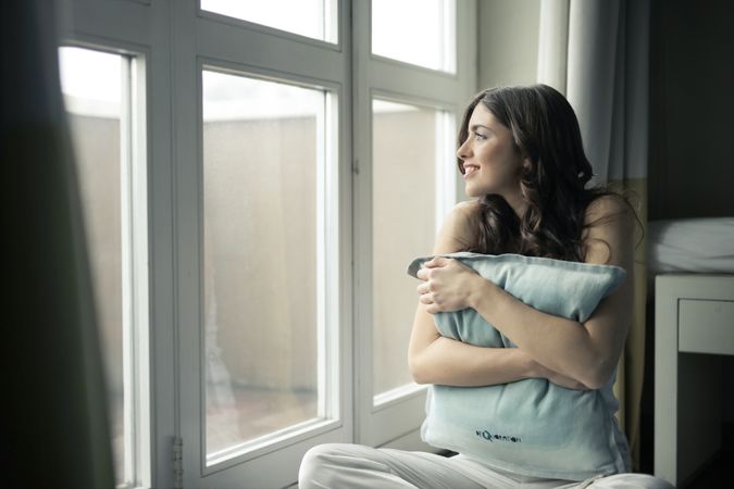 Black Haired Woman Hugging Gray Pillow Near Glass-panel Window Photo