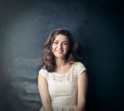 Brown Haired Girl In White Sleeveless Dress Standing Beside Black Painted Wall Photo