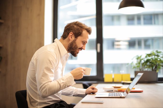 Man Holding Teacup Infront Of Laptop On Top Of Table Inside The Room Photo