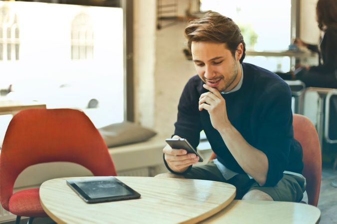 Man In Black Sweater Holding Smartphone While Sitting On Chair Photo
