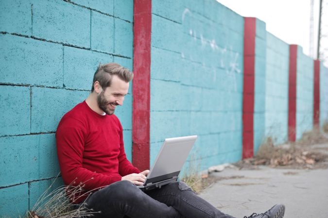 Man Leaning Against Blue Wall Using Laptop Photo