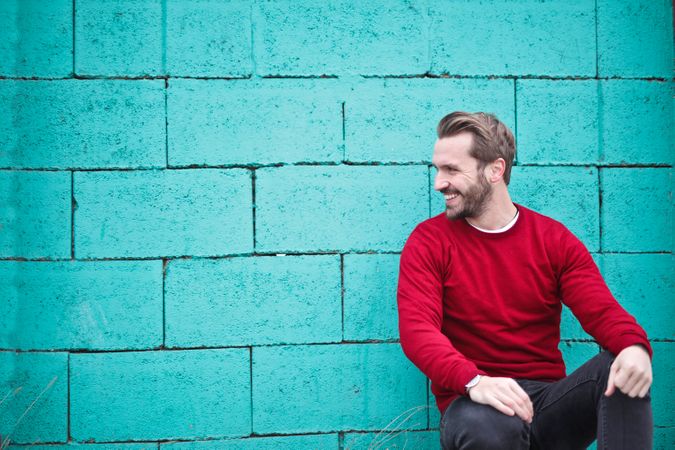Man Wearing Red Sweatshirt And Black Pants Leaning On The Blue Wall Photo