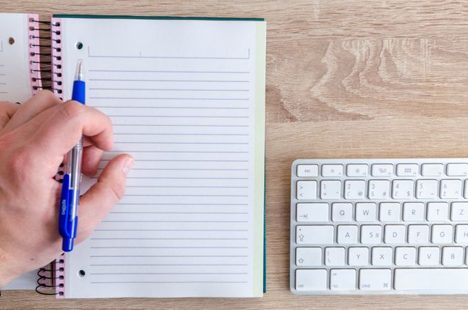 Person Is Ready To Write On Notebook Beside White Keyboard Photo