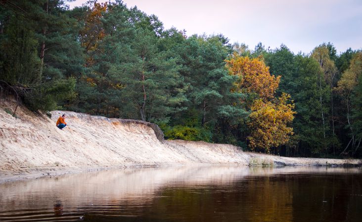 Person Seated Facing Body Of Water In Forest Photo
