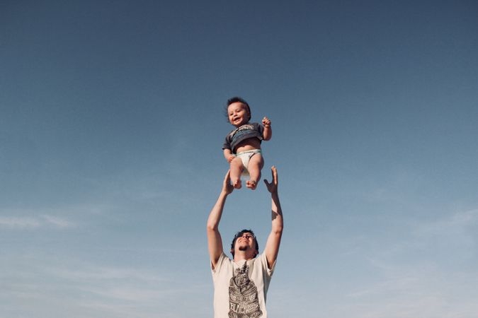 Photo Of Man In Raising Baby Under Blue Sky Photo