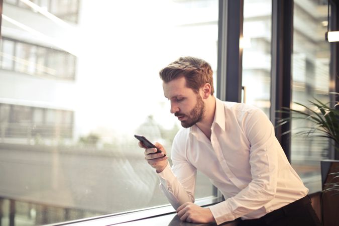 Photo Of Man In White Dress Shirt Holding Phone Near Window Photo