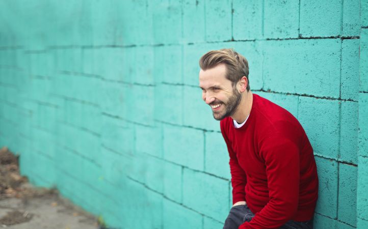 Smiling Man Wearing A Red Sweater Leaning On A Blue Wall Photo