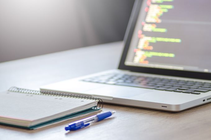 Spiral Notebook And Blue Pen Beside Mac-book Photo