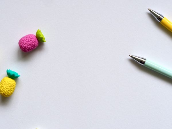 Two Purple And Yellow Pineapple Erasers Near Pens Photo