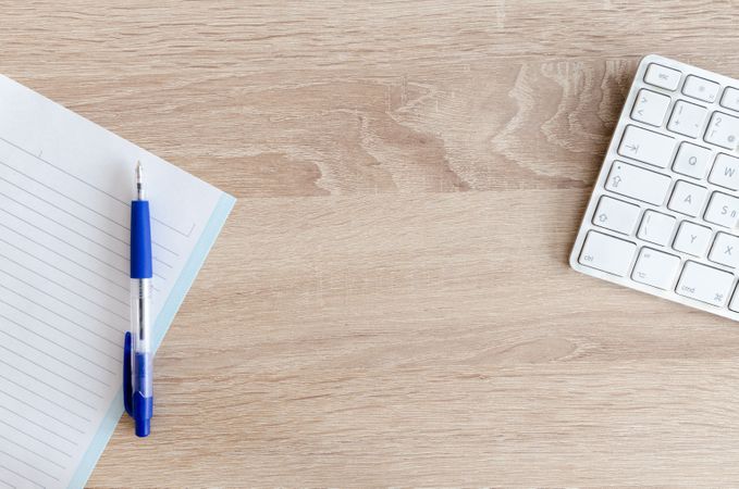 White Keyboard And Notebook With Blue Pen On Wooden Table Photo