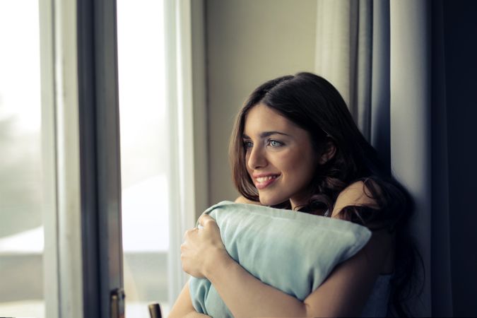 Woman Hugging White Pillow Beside Glass Door Photo