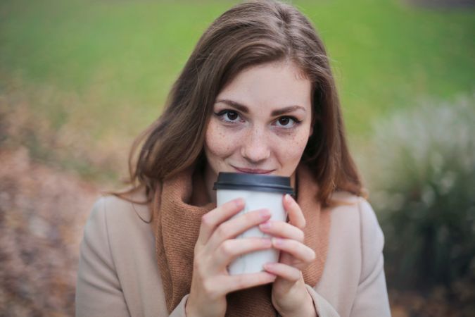 Woman In Brown Top And Scarf Holding A White And Black Travel Cup Outside Photo