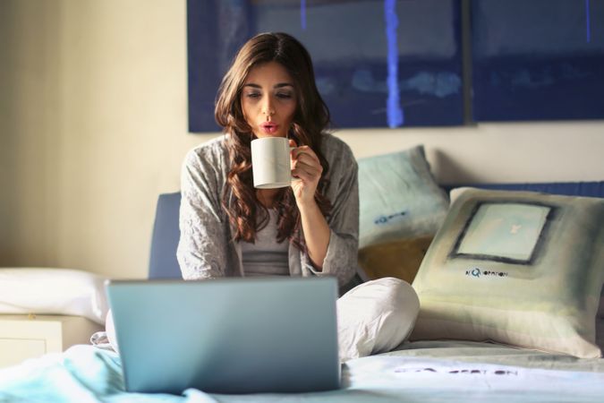 Woman In Grey Jacket Sits On Bed Uses Grey Laptop Photo