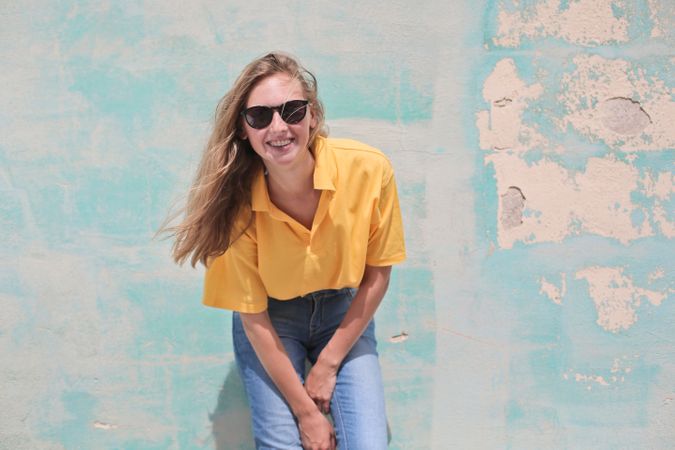 Woman Wearing Yellow Polo Shirt Standing In Front Of Teal Concrete Wall Photo