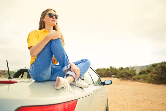 Woman Wears Yellow Shirt And Blue Denim Jeans Sits On Silver Car Photo