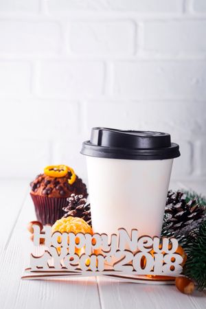 Paper Cup Of Coffee With Muffin, Pine Cone And Mandarin Surrounded By Lettering Happy New Year On White Wooden Background Photo
